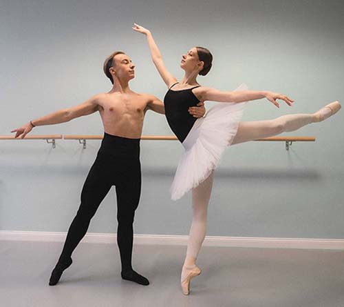 Pas de deux w sali baletowej: tancerz i baletnica w białej tutu na pointach przy drążku